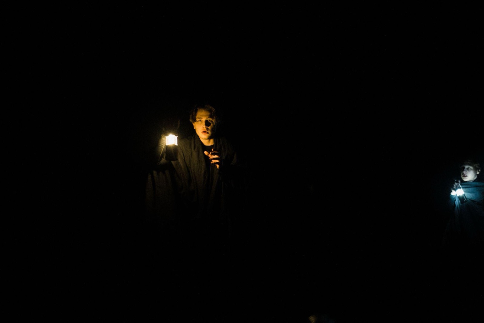 Hryhorii on a dark stage, lit only by the lantern he holds