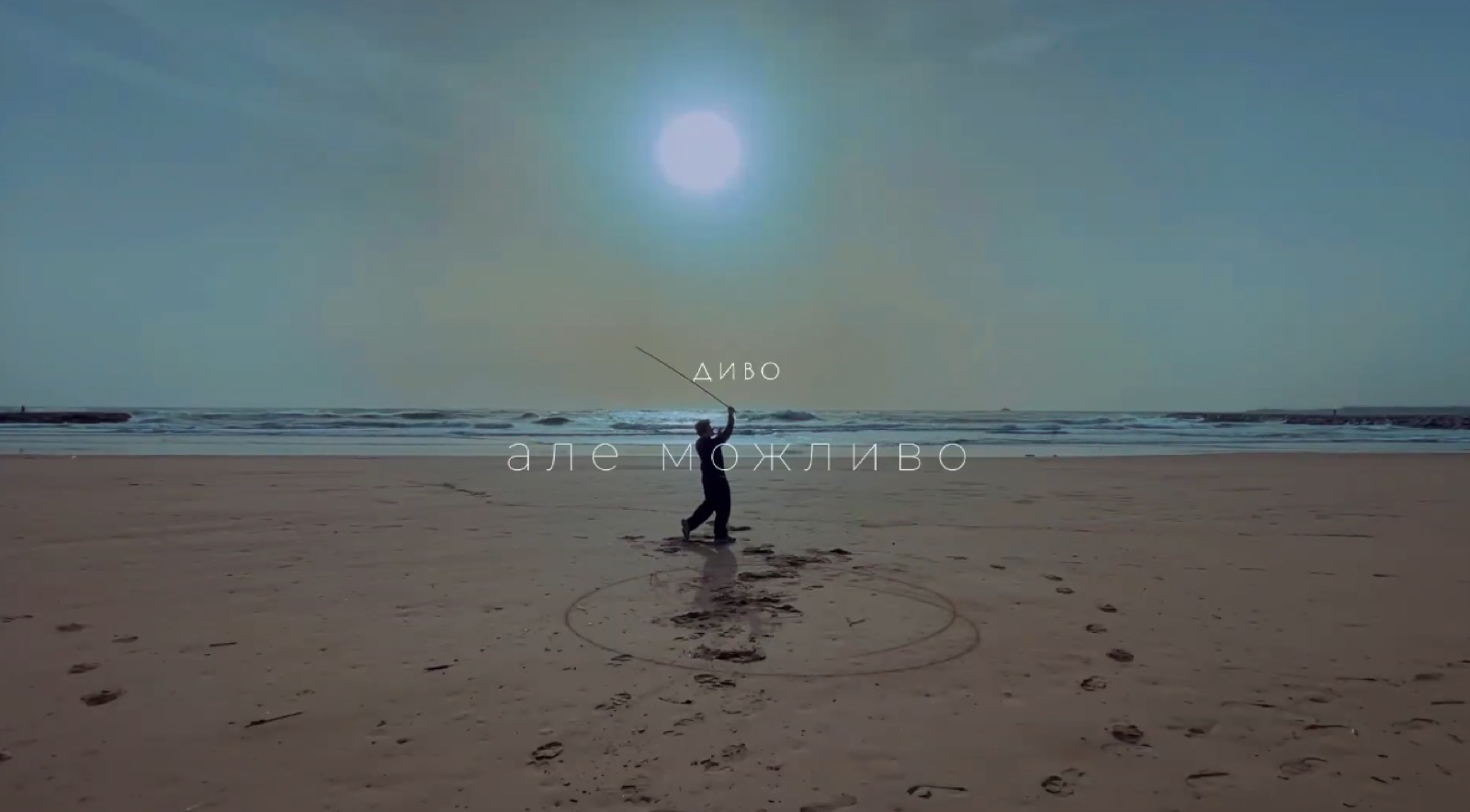 A lone figure drawing a circle on a beach, music video still